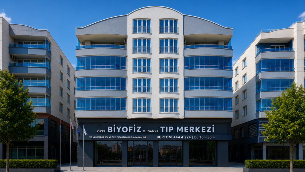 Front view of a modern medical center with blue-tinted glass windows and curved balconies, signage reads Özel Biyofiz Mudanya Tıp Merkezi.