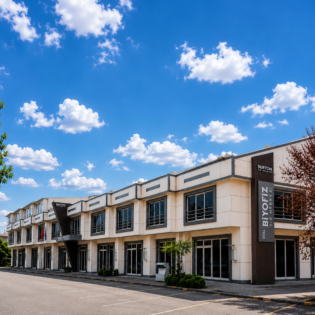 Modern multi-story commercial building with large windows, set against a bright blue sky with scattered clouds.