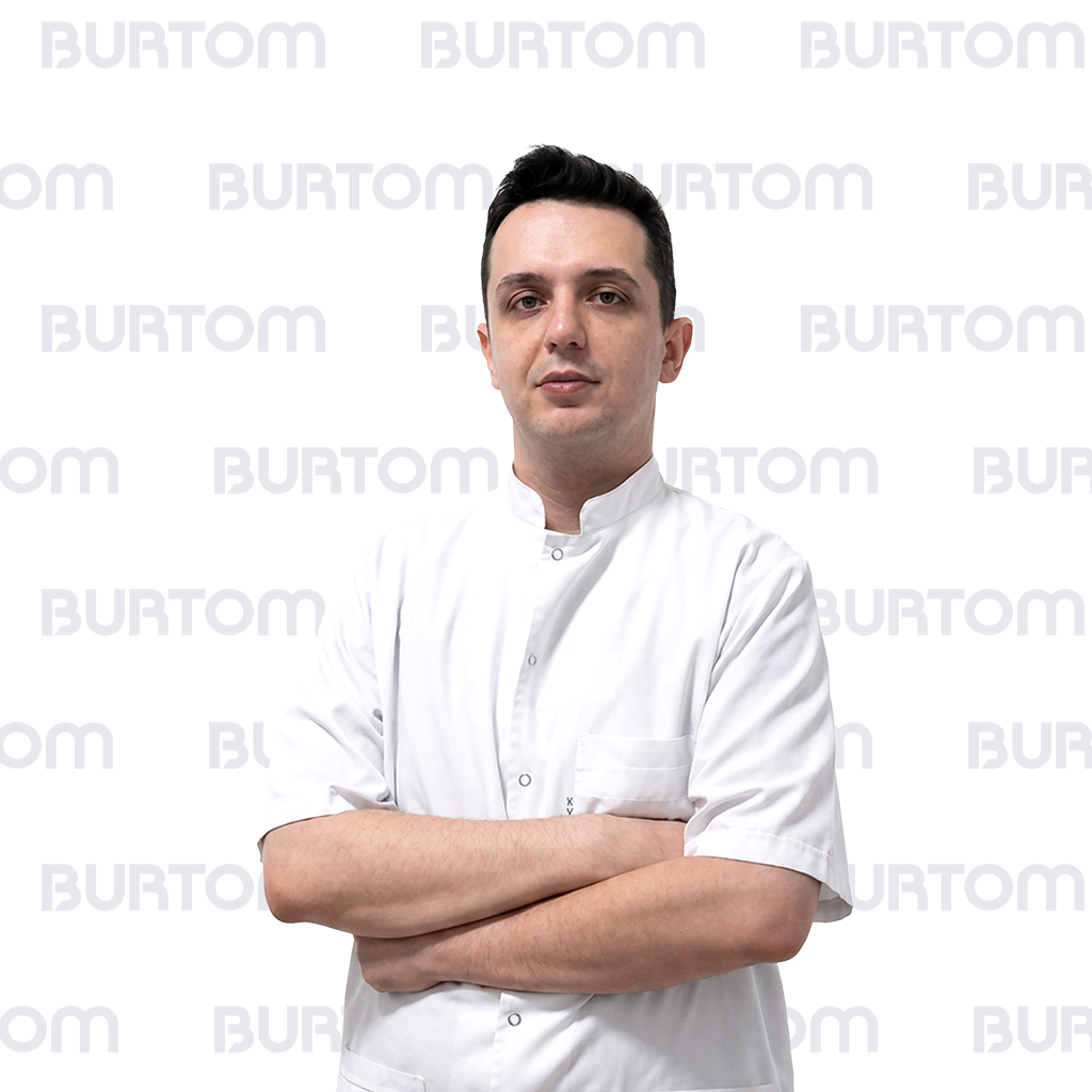 Male healthcare professional in a white uniform, arms crossed, looking at the camera.